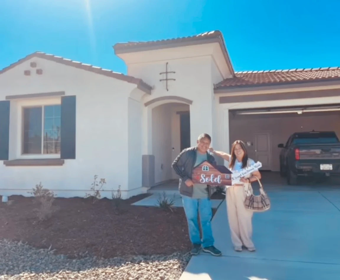 Filipino couple in front of their new home with sold sign